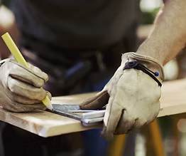 Person wearing gloves using a tool on a wooden surface