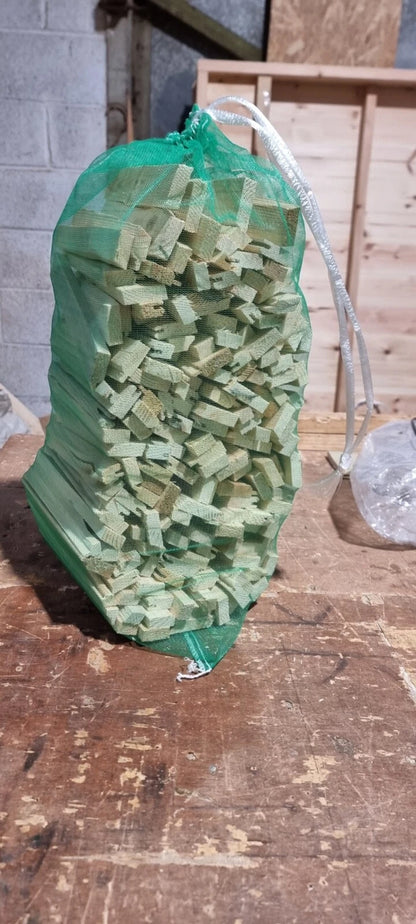 Bag of green wooden planks on a wooden surface with a concrete wall in the background.